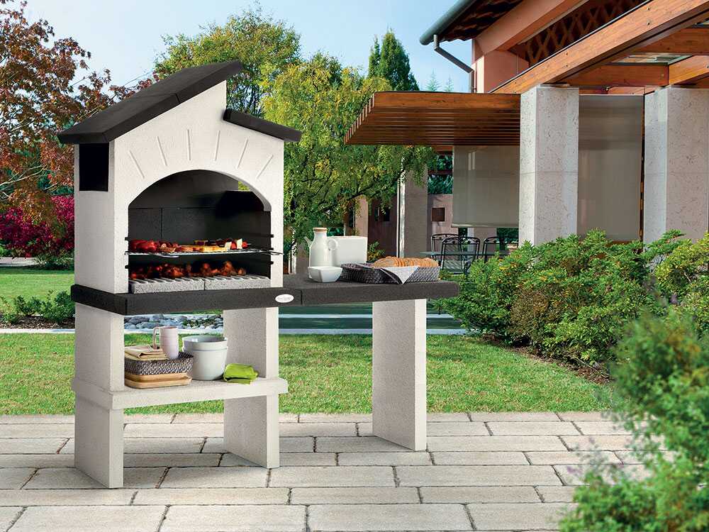 Barbecue à bois et charbon Palazzetti Ravello en ciment réfractaire avec grille réglable 68 x 40 cm, espaces de rangement et finitions Marmotech. Idéal pour 10 à 14 personnes.